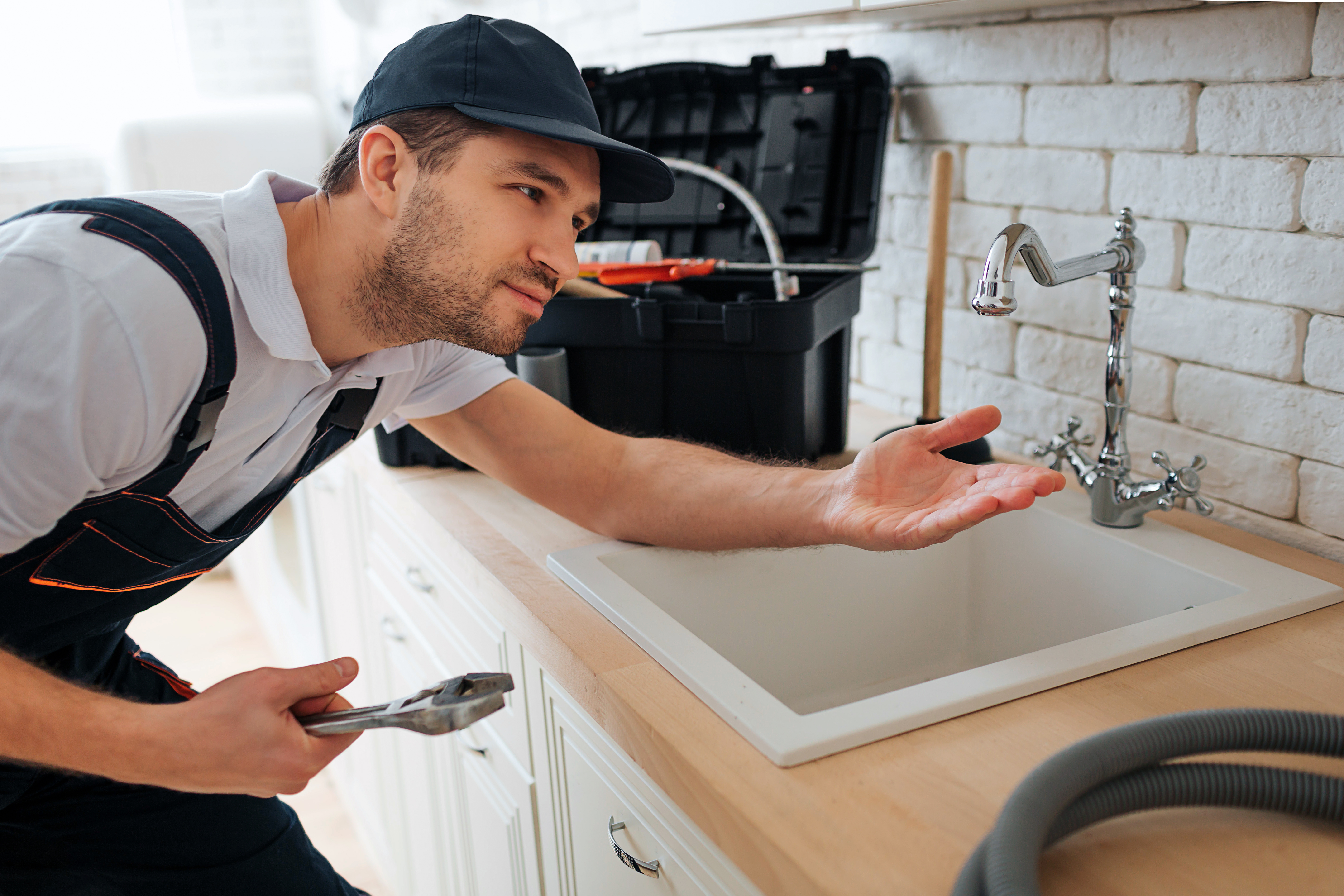 DIY sink repair in action – a man unclogging a kitchen sink with common tools Man using tools to repair a clogged kitchen sink